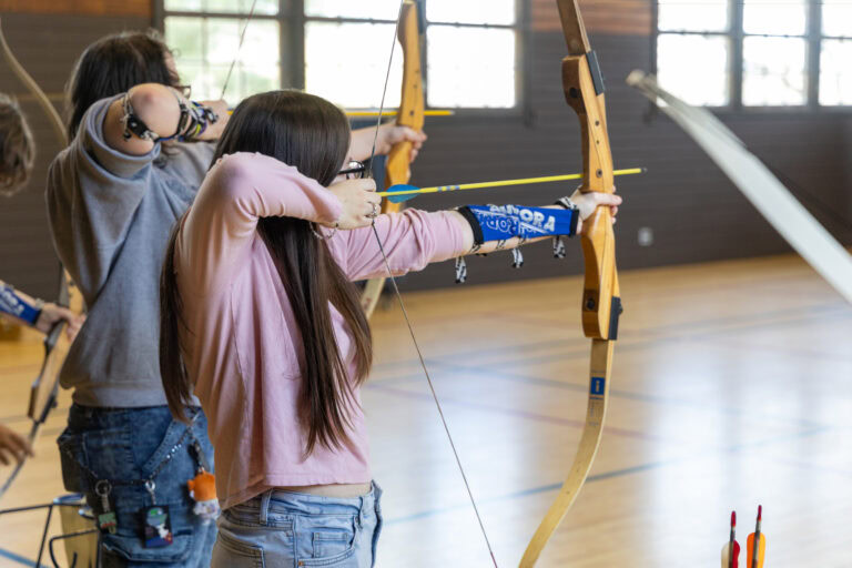 Teen aims bow and arrow at target.
